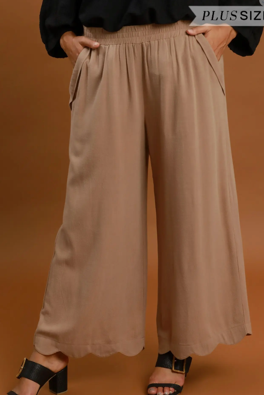A person wearing wide-leg taupe pants with an elastic waistband, paired with a black top and black heeled sandals, against a solid brown background.