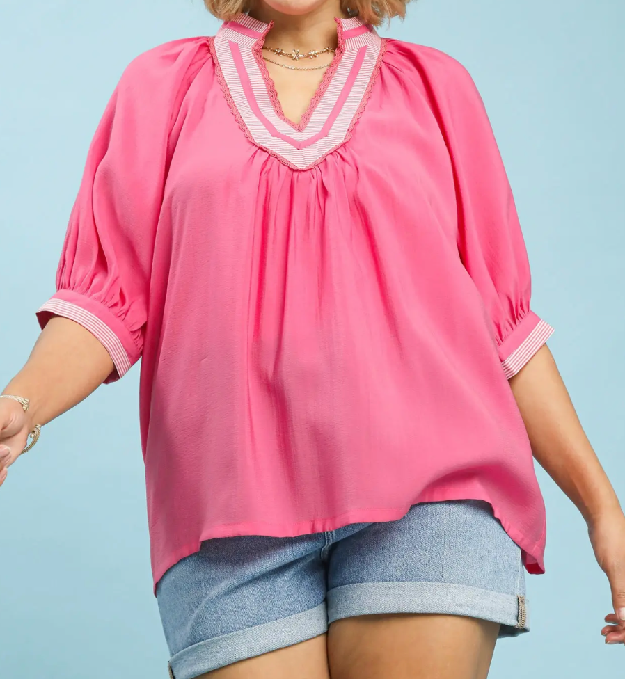 Person wearing a pink blouse with white trim and denim shorts on a light blue background